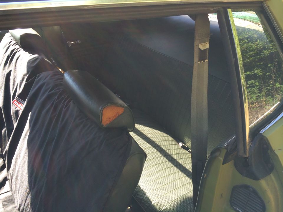Interior view of green seats with a black cover and exposed foam on headrest