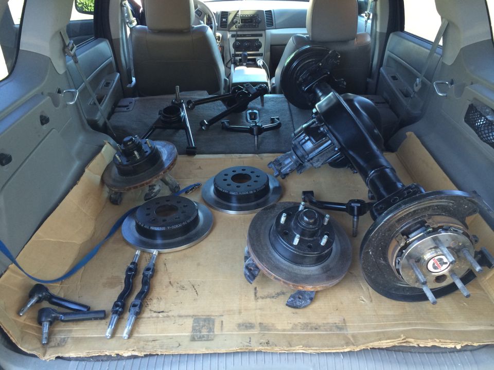 Various car parts including axles, brake rotors, and suspension components laid out on cardboard in the cargo area of an SUV