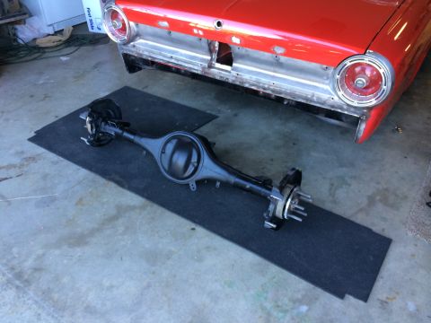 1964 Ford Fairlane - A rear axle assembly is shown in front of a red car that appears to be undergoing restoration.