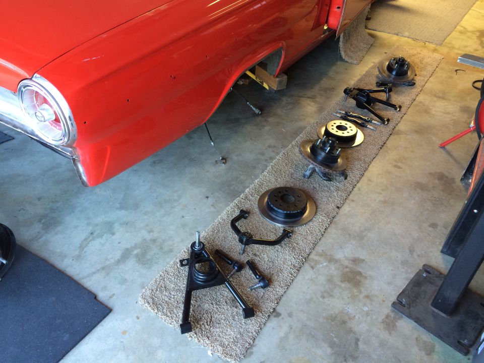 Red 1964 Ford Fairlane side view, showing disassembled front suspension components laid out on a rug