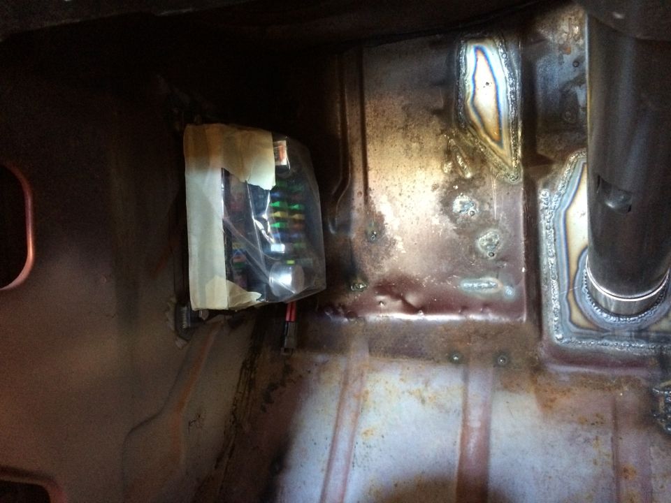 Fuse box wrapped in plastic and taped to metal panel with visible wiring