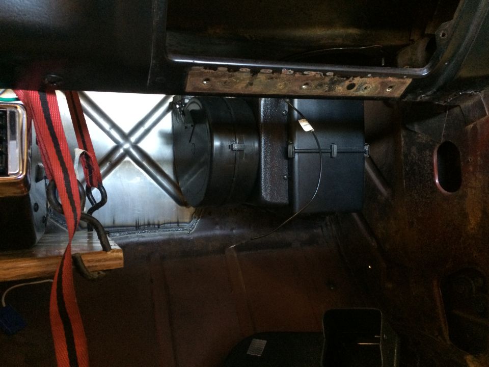Interior view of a vehicle's dashboard area with a red seatbelt, HVAC unit, and metal bracing