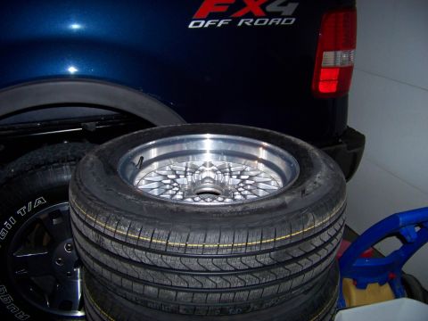 1999 Mercury Grand Marquis - Custom wheel and tires stacked in front of a pickup truck's fender.