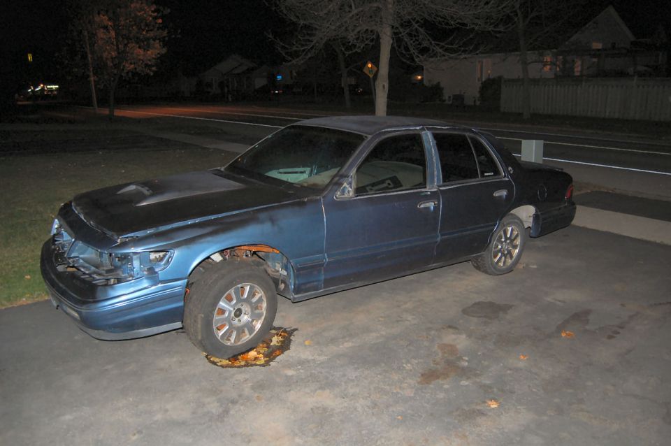 Blue sedan with damaged front end and missing grille, parked on driveway