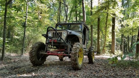 Modified jeep with large tires on a muddy forest trail