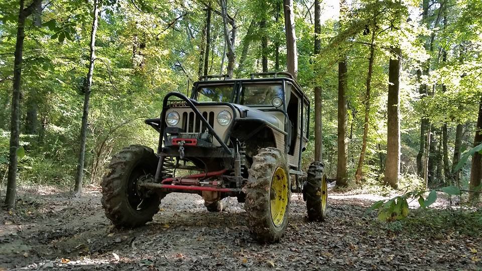 Modified jeep with large tires on a muddy forest trail