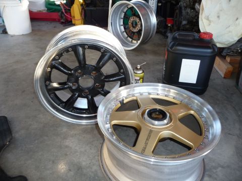 1993 Mazda MX-3 - A gold Mazdaspeed wheel is shown alongside two other aftermarket wheels and a can of spray lubricant.