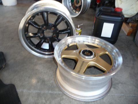 1993 Mazda MX-3 - A pair of aftermarket wheels are displayed on a concrete surface, with a fuel jug and spray can in the background.