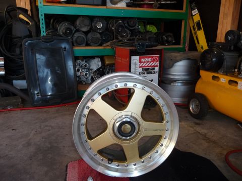 1993 Mazda MX-3 - A single gold alloy wheel with a silver lip is displayed in a workshop setting.