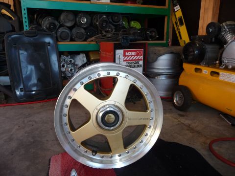 1993 Mazda MX-3 - Aftermarket wheel with gold spokes and silver lip sits in a garage.