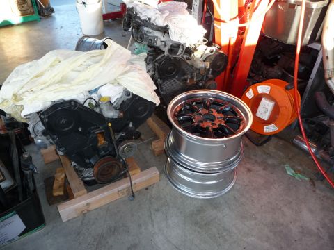1993 Mazda MX-3 - Two automotive engines and a set of three custom wheels are stored indoors, possibly in a garage or workshop.