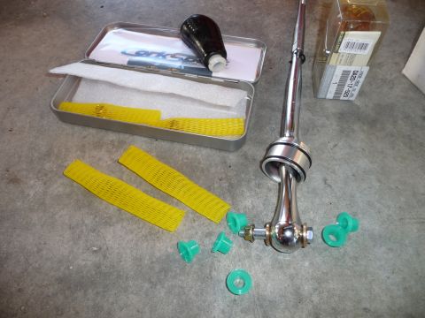 1993 Mazda MX-3 - A short shifter kit is laid out on a concrete surface, including a chrome shifter, black shift knob, and green bushings.