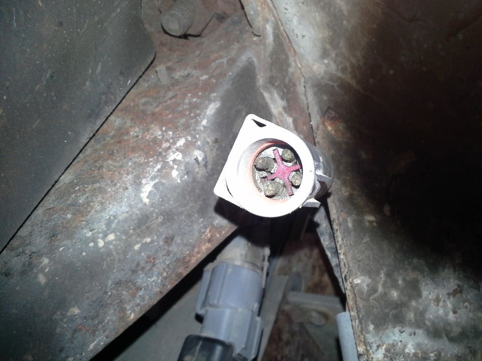 Electrical connector with four pins and a pink cross-shaped insert, attached to a rusty metal frame
