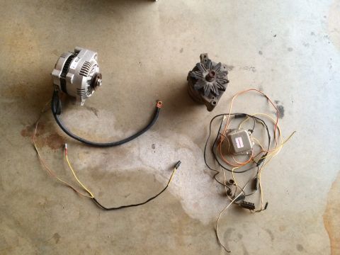 1977 Ford F-350 - Comparison of an older and newer alternator, along with associated wiring components, displayed on a concrete surface.
