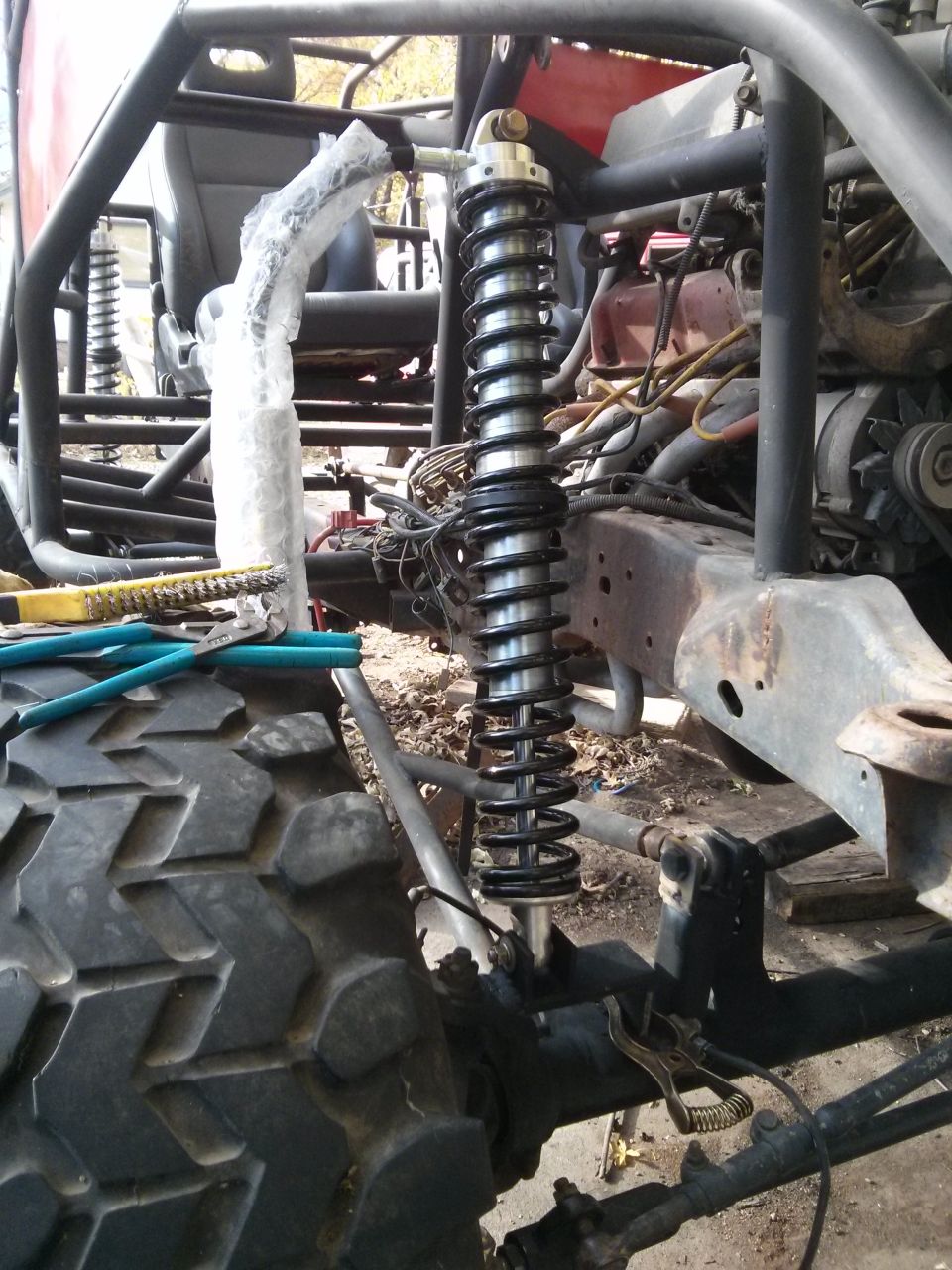 Off-road vehicle chassis with large tire, coilover shock, and roll cage. Tools are on the tire