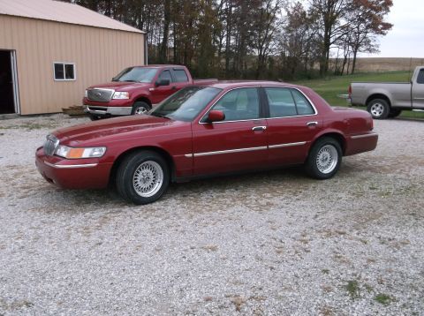 1999 Mercury Grand Marquis - Red 1999 Mercury Grand Marquis sedan with aftermarket wheels parked outside a building.