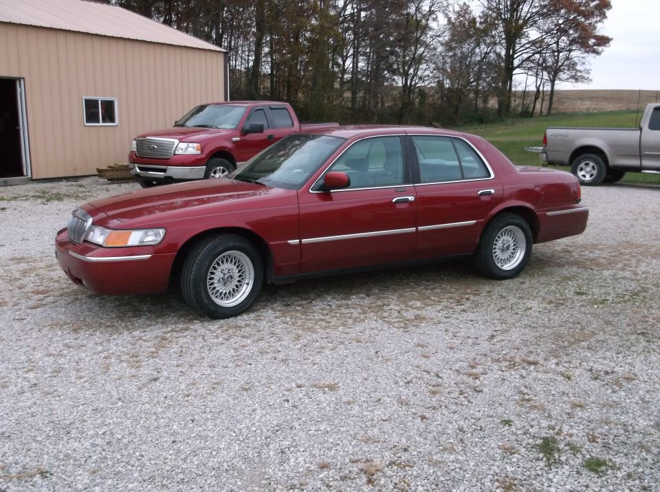 1999 Mercury Grand Marquis sedan parked on gravel lot, red pickup truck behind it