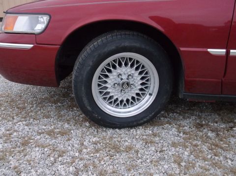1999 Mercury Grand Marquis - Close-up of the front wheel and fender of a red Mercury Grand Marquis.