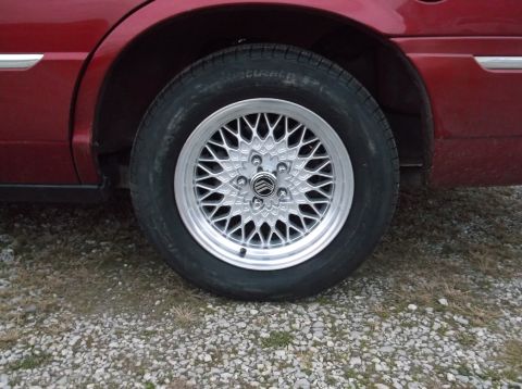 1999 Mercury Grand Marquis - Close-up of a 1999 Mercury Grand Marquis wheel a silver mesh rim and the Mercury logo on the hub.