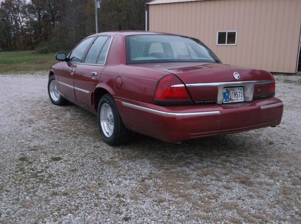 1999 Mercury Grand Marquis, rear 3/4 view, red paint, chrome trim, aftermarket wheels