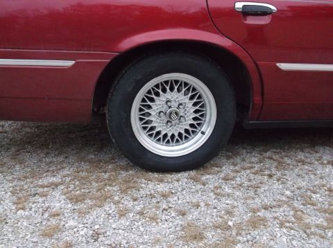 1999 Mercury Grand Marquis - The rear wheel of a red 1999 Mercury Grand Marquis features a mesh alloy rim.