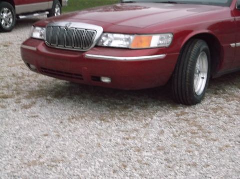 1999 Mercury Grand Marquis - Front view of a red sedan with a chrome grille and chrome bumper trim, parked on a gravel surface.