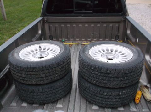 1999 Mercury Grand Marquis - Four tires and wheels are stacked in the bed of a pickup truck.