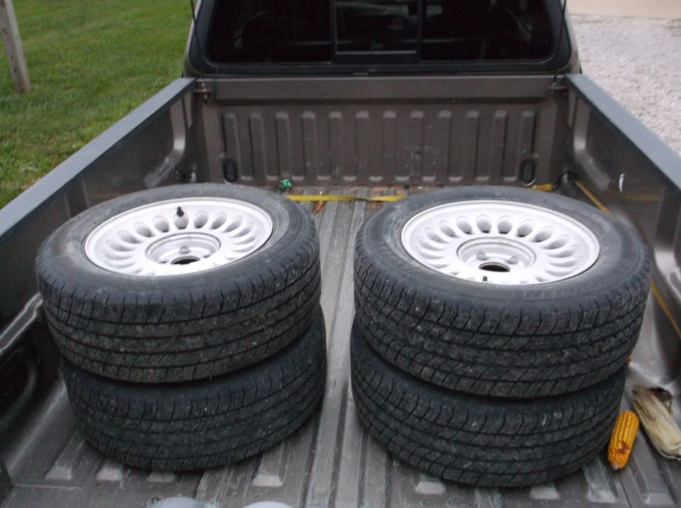 four tires stacked on silver alloy wheels in a pickup truck bed