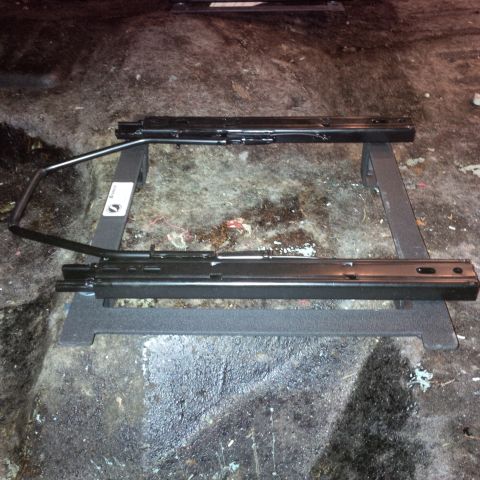 1978 Ford Bronco - Black metal seat sliders are shown on a dark, dirty floor.