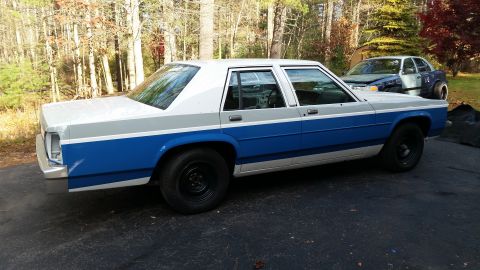 1991 Ford LTD Crown Victoria - A two-tone sedan with blue and gray stripes is parked outside, with another vehicle in the background.