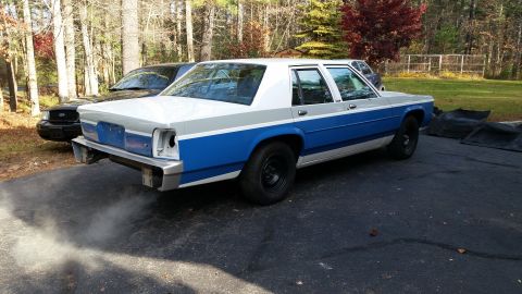 1991 Ford LTD Crown Victoria - A two-tone blue and white Ford Crown Victoria is parked outside, with a black vehicle in the background.