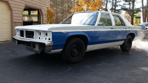 1991 Ford LTD Crown Victoria - This car appears to be undergoing some restoration work, with its front end partially disassembled and smoke coming from the exhaust pipe.