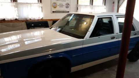 1991 Ford LTD Crown Victoria - A white and blue two-tone 1991 Ford Crown Victoria LTD sedan is viewed from the front 3/4 angle inside a garage.