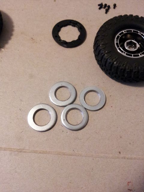 1995 Ford Bronco - Parts for an RC car, including a tire, wheel, and several washers, are laid out on a surface.