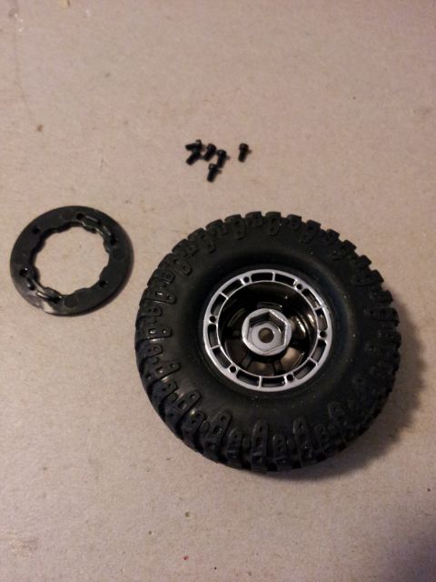1995 Ford Bronco - A disassembled RC car tire and wheel assembly lies on a textured surface next to its mounting hardware.
