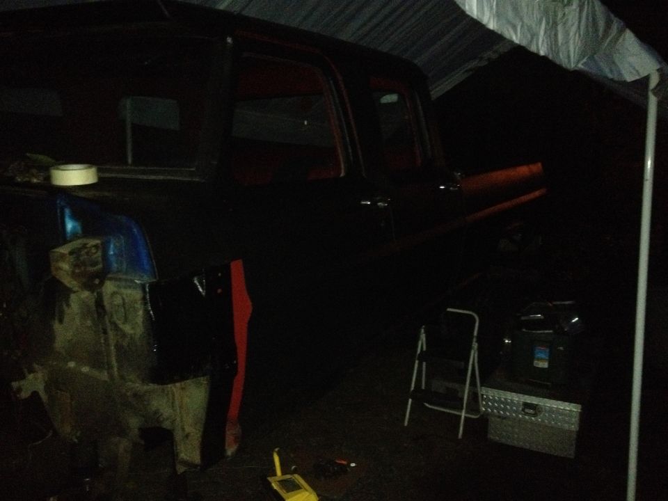 Truck cab and front fender area visible under a tarp, with tools and a ladder nearby