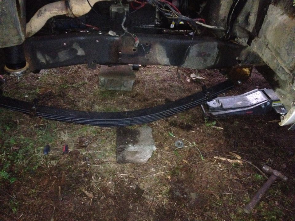 Rear leaf spring resting on concrete blocks under a truck chassis at night