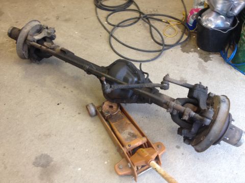 1971 Ford F-250 - Front axle assembly with drum brakes and steering linkage, supported by a floor jack.