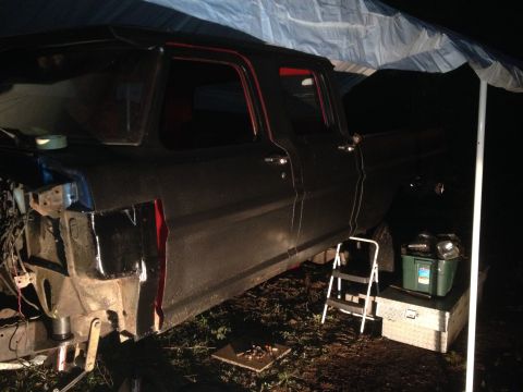 1971 Ford F-250 - A dark-colored pickup truck is parked under a tarp with a step ladder and toolboxes next to it.