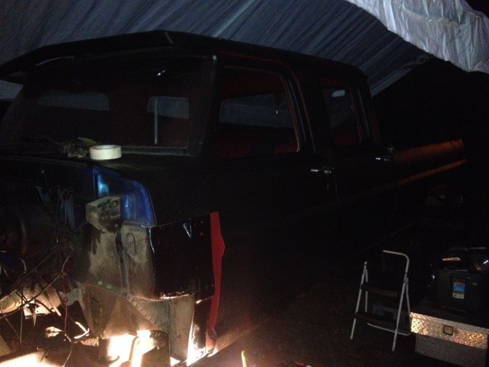 Side view of a dark pickup truck undergoing repairs, showing exposed metal and red trim