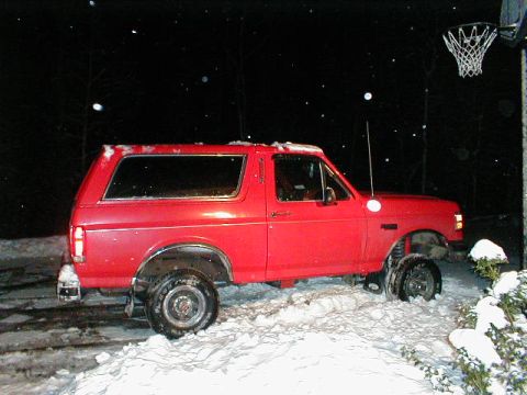 1990 Ford Bronco - A red 1990 Ford Bronco with a lifted suspension is parked in the snow at night.