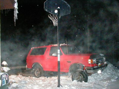 1990 Ford Bronco - A red 1990 Ford Bronco is partially buried in snow, with icicles hanging from an overhang.