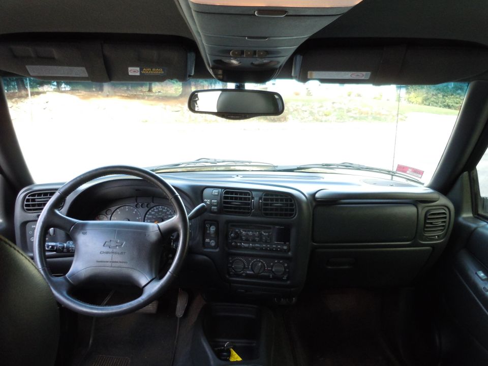 Chevrolet Blazer interior with dashboard, steering wheel, and center console visible. Airbag warning labels on sun visors