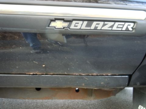 2001 Ford Crown Victoria - Close-up of a Chevrolet Blazer badge on the side of a vehicle, with visible rust on the lower panel.
