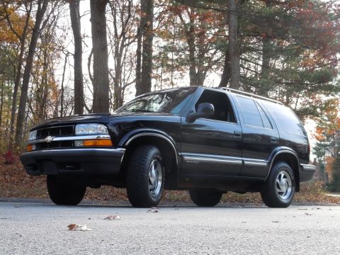2001 Ford Crown Victoria - This black SUV is parked on the side of a road with autumn trees in the background.