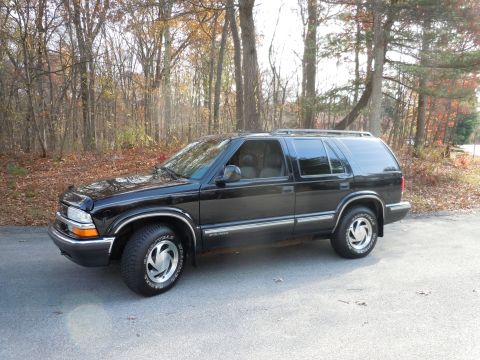 2001 Ford Crown Victoria - A black SUV is parked on a road with autumn foliage visible in the background.