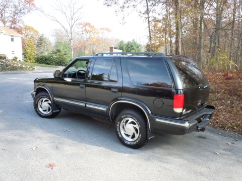 2001 Ford Crown Victoria - Black SUV parked on a paved surface with trees and a house in the background.
