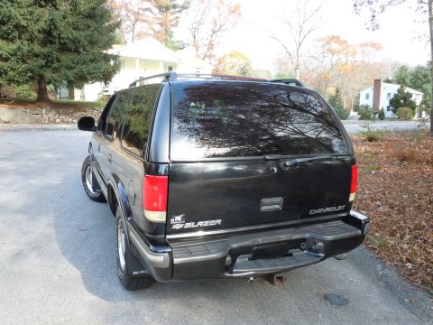 2001 Ford Crown Victoria - Rear view of a black Chevrolet Blazer SUV parked on a paved surface with trees and houses in the background.