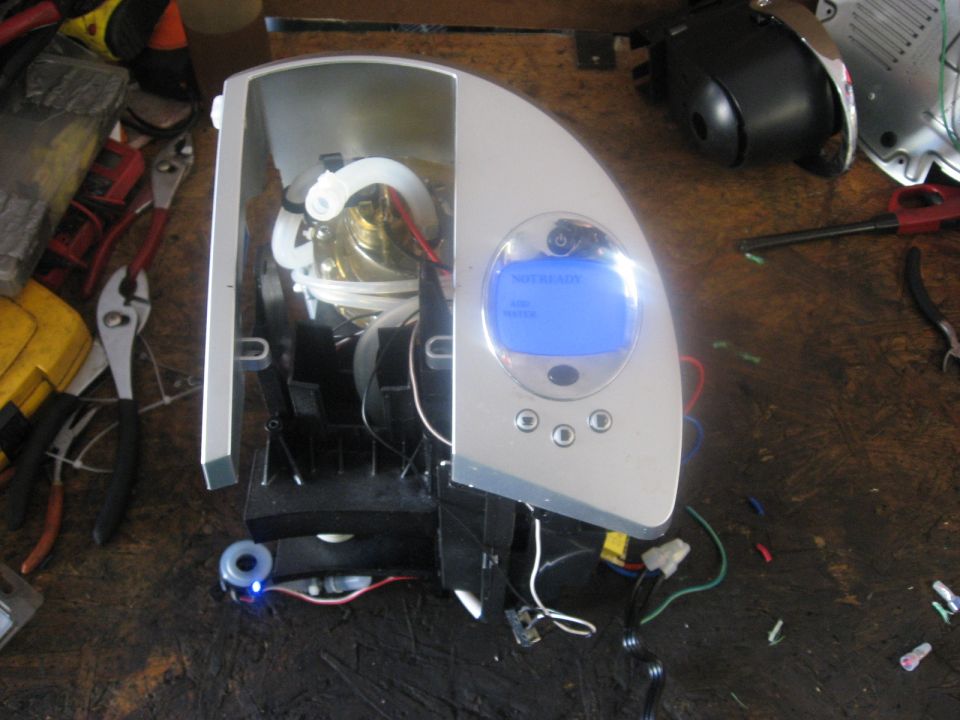 Silver and white coffee maker disassembled on a wooden workbench with tools