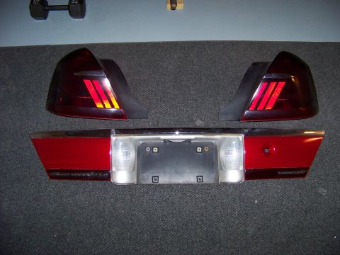 1999 Mercury Grand Marquis - 1999 Mercury Grand Marquis tail lights and rear trim panel are laid out on a carpeted surface.